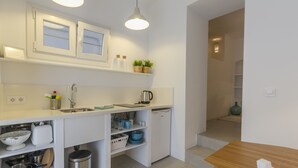 Una cocina compacta con armarios blancos, un lavamanos, una cafetera y un cubo de basura pequeño.