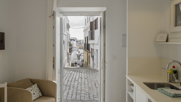 Un estrecho pasillo que da a una calle empedrada, con un sofá y un lavabo a la izquierda.