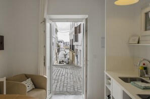 En smal gang der fører til en brostensbelagt gade, med en sofa og en vask synlige på venstre side.