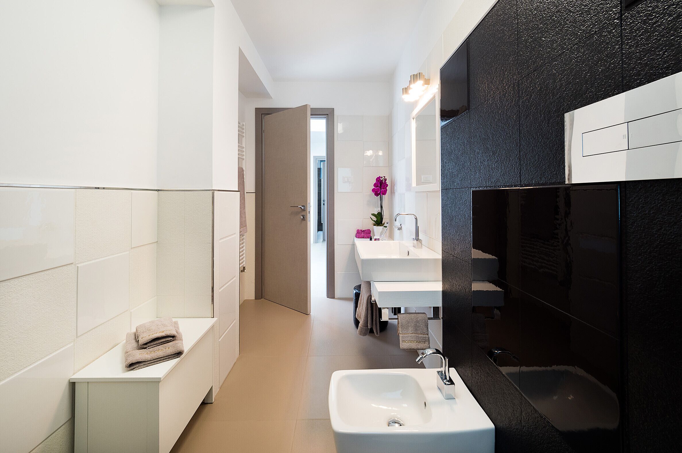 A modern bathroom with a white vanity, a large mirror, and a black textured wall.
