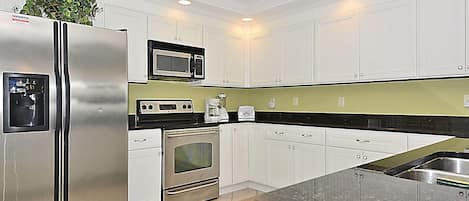 A modern kitchen with white cabinets, stainless steel appliances, a black countertop, and a green backsplash.