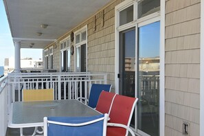 A covered outdoor seating area with a table and chairs, a railing, and a view of the surrounding buildings.