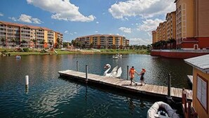 A waterfront hotel with a dock, swans, and a person walking.