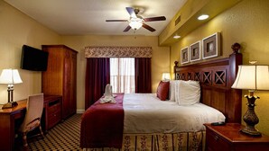 A hotel room with a bed, a desk, a chair, a television, a ceiling fan, and a window with curtains.