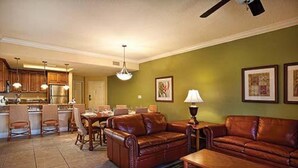A living room with a brown leather sofa, a coffee table, and a dining area with a table and chairs.
