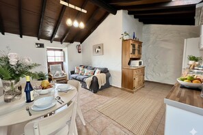 Un comedor con una mesa dispuesta para dos personas, un sofá, un armario y una zona de cocina con microondas.