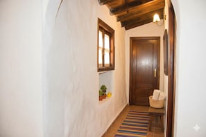 A hallway with a wooden door, a small shelf with plants, a bench, and a colorful striped rug.