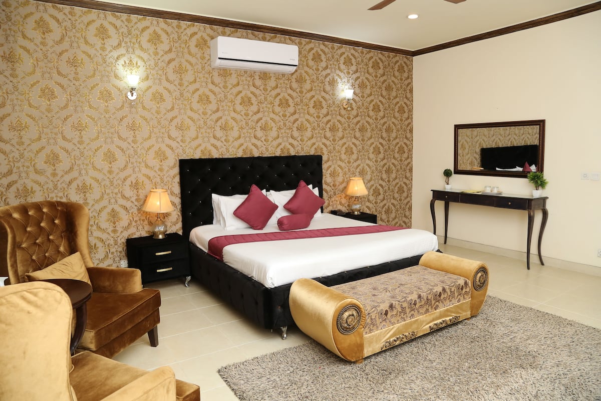 A bedroom with a large bed, two bedside tables, a chair, a desk, and a mirror.