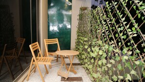 A patio area with wooden chairs and a table, a green wall with climbing plants, and a glass door leading inside. - The Westin Suites Hotel (Lahore)