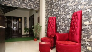 A lobby with a stone wall, a red upholstered sofa, a small round ottoman, and a potted plant. - The Westin Suites Hotel (Lahore)