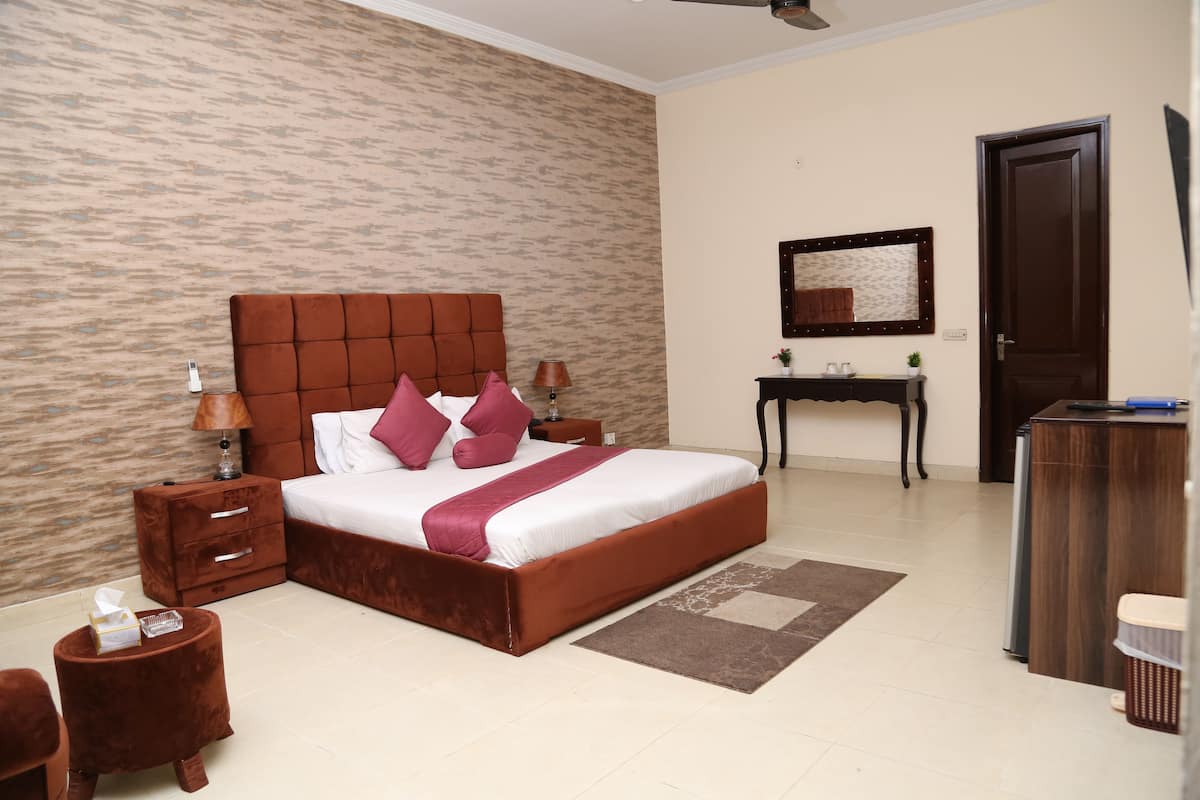 A bedroom with a large bed, a nightstand, a bedside table, a dresser, and a mirror on the wall.