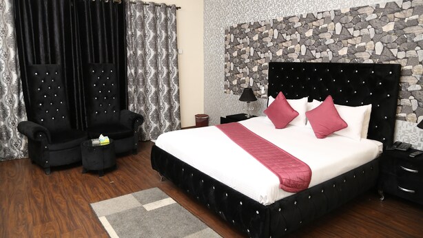 A bedroom with a large bed, two black armchairs, a small side table, and a stone wall. - The Westin Suites Hotel (Lahore)