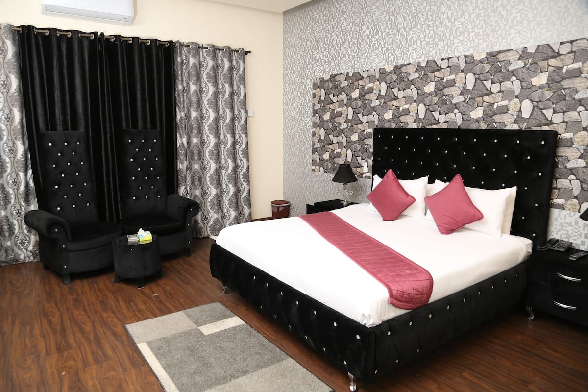 A bedroom with a large bed, two black armchairs, a small side table, and a stone wall.