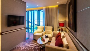 A modern hotel room with a flat-screen TV, a sofa, two armchairs, a small table with fruit, and a view through large windows. - VIP Hotel (Doha)