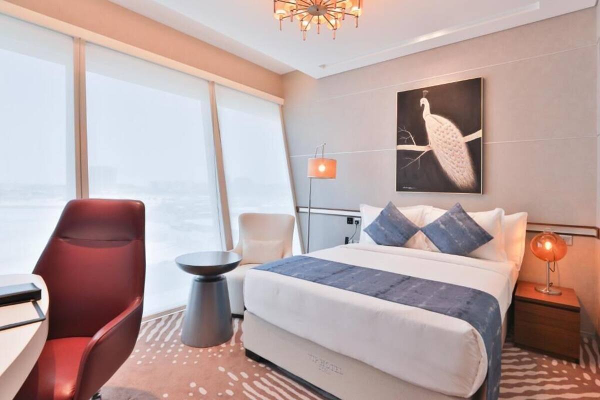 A hotel room with a large bed, a red chair, a small table, and a large window.