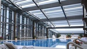An indoor swimming pool with lounge chairs and potted plants.