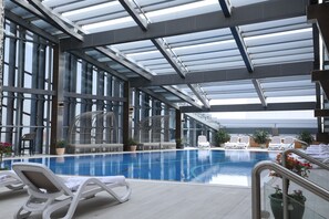 An indoor swimming pool with lounge chairs and potted plants.