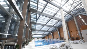 An indoor swimming pool with lounge chairs and a glass ceiling. - VIP Hotel (Doha)