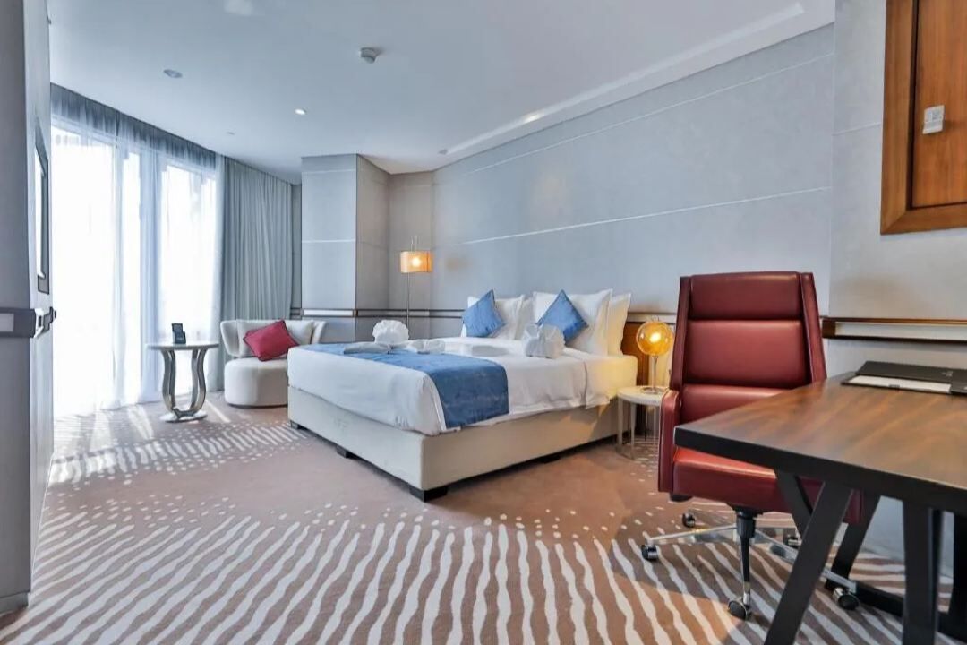 Habitació d'hotel moderna amb un llit gran, una cadira de pell vermella, una taula petita i una làmpada.