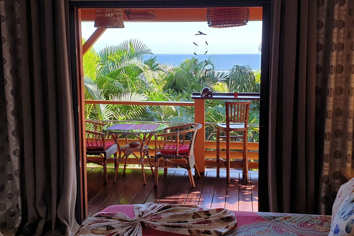 Ein Balkon mit Tisch und Stühlen mit Blick auf einen üppigen Garten und das Meer.