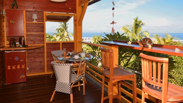 A wooden interior with a dining area, a bar, and a view of the beach. - Poz Lagon (Saint-Paul)