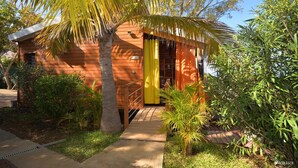 A wooden cabin with a yellow door, surrounded by lush greenery and palm trees. - Poz Lagon (Saint-Paul)