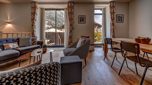 A modern living room with a sofa, armchair, ottoman, and dining area with chairs. - Central Duplex Apartment with Large Terrace (Chamonix-Mont-Blanc)