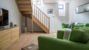 A modern living room with a staircase, green sofa, wooden cabinets, and a flat-screen TV. - Central Duplex Apartment with Large Terrace (Chamonix-Mont-Blanc)