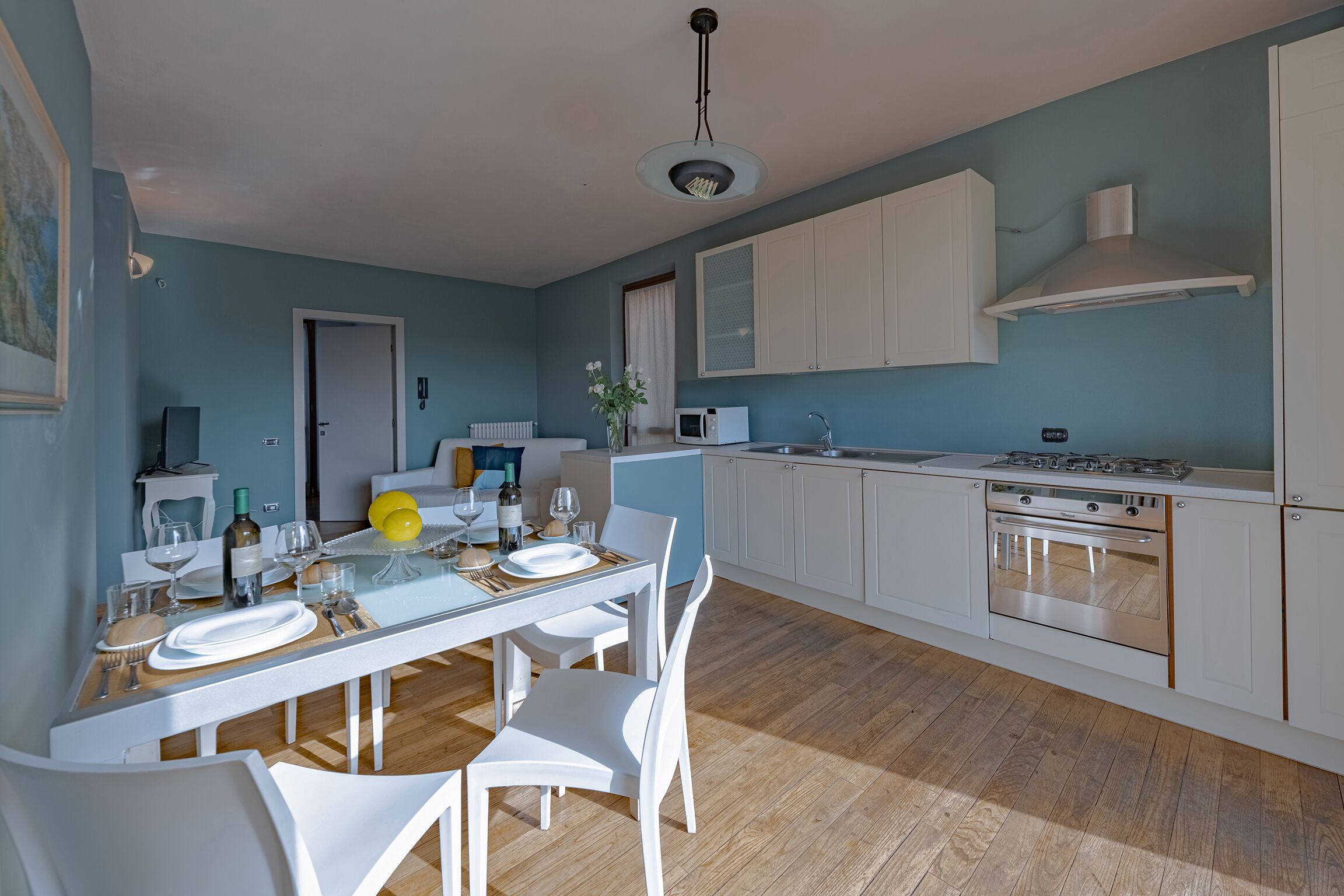 A modern kitchen with white cabinets, a stainless steel oven, and a dining area with a glass table and white chairs.