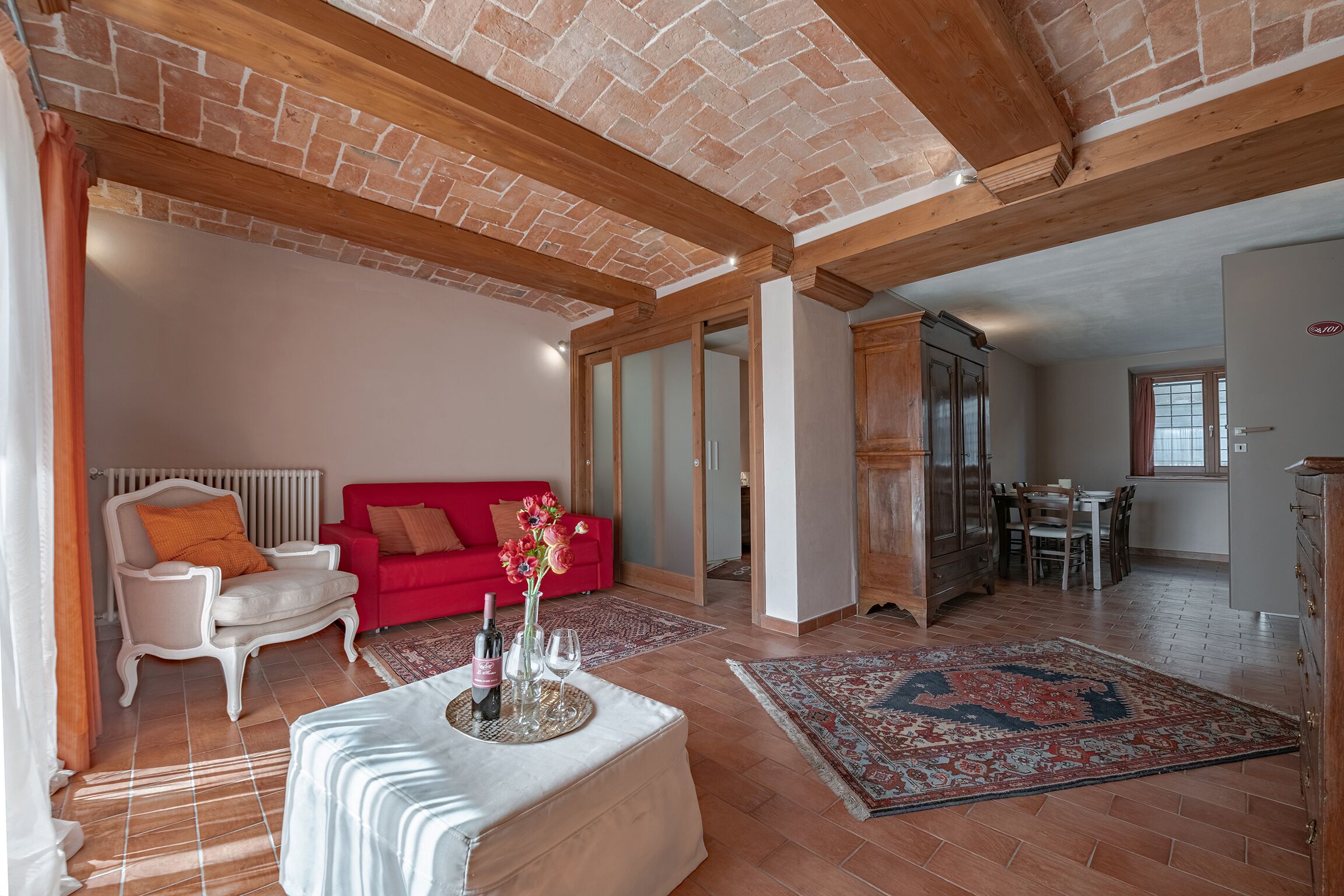 Amplia sala de estar con un sofá rojo, un sillón blanco y una mesa de comedor con sillas.