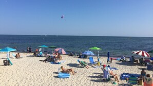 Una spiaggia con persone che prendono il sole e nuotano, ombrelloni e cielo sereno.