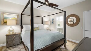 Ein Himmelbett mit Moskitonetz, ein Nachttisch mit Lampe, eine Kommode und eine Wand mit gerahmten Kunstwerken.