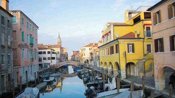 A canal with boats docked, a bridge, and buildings with arched windows and balconies. - Casa Bastianello large apartment, view of Canal Vena Historic Center comfort (Chioggia)