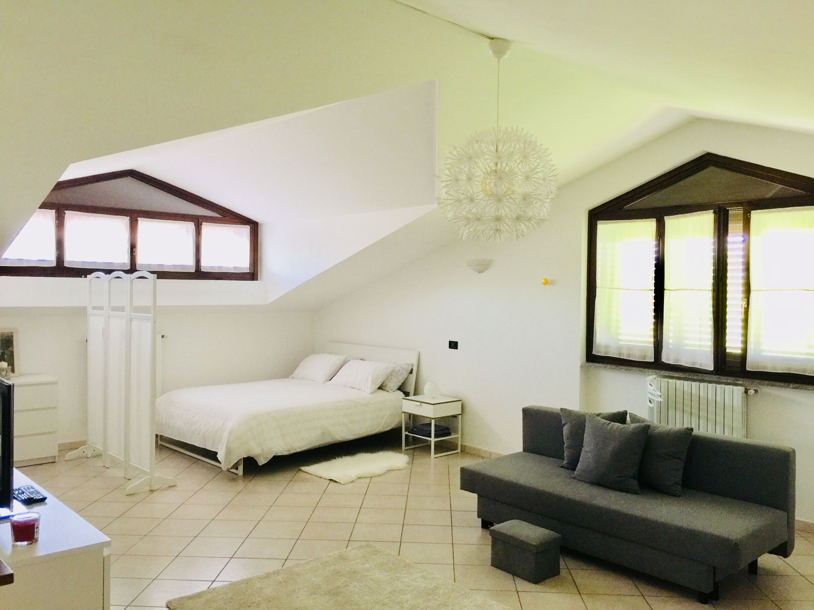 Een slaapkamer met een bed, een grijze bank, een klein tafeltje en een raam met zonwering.