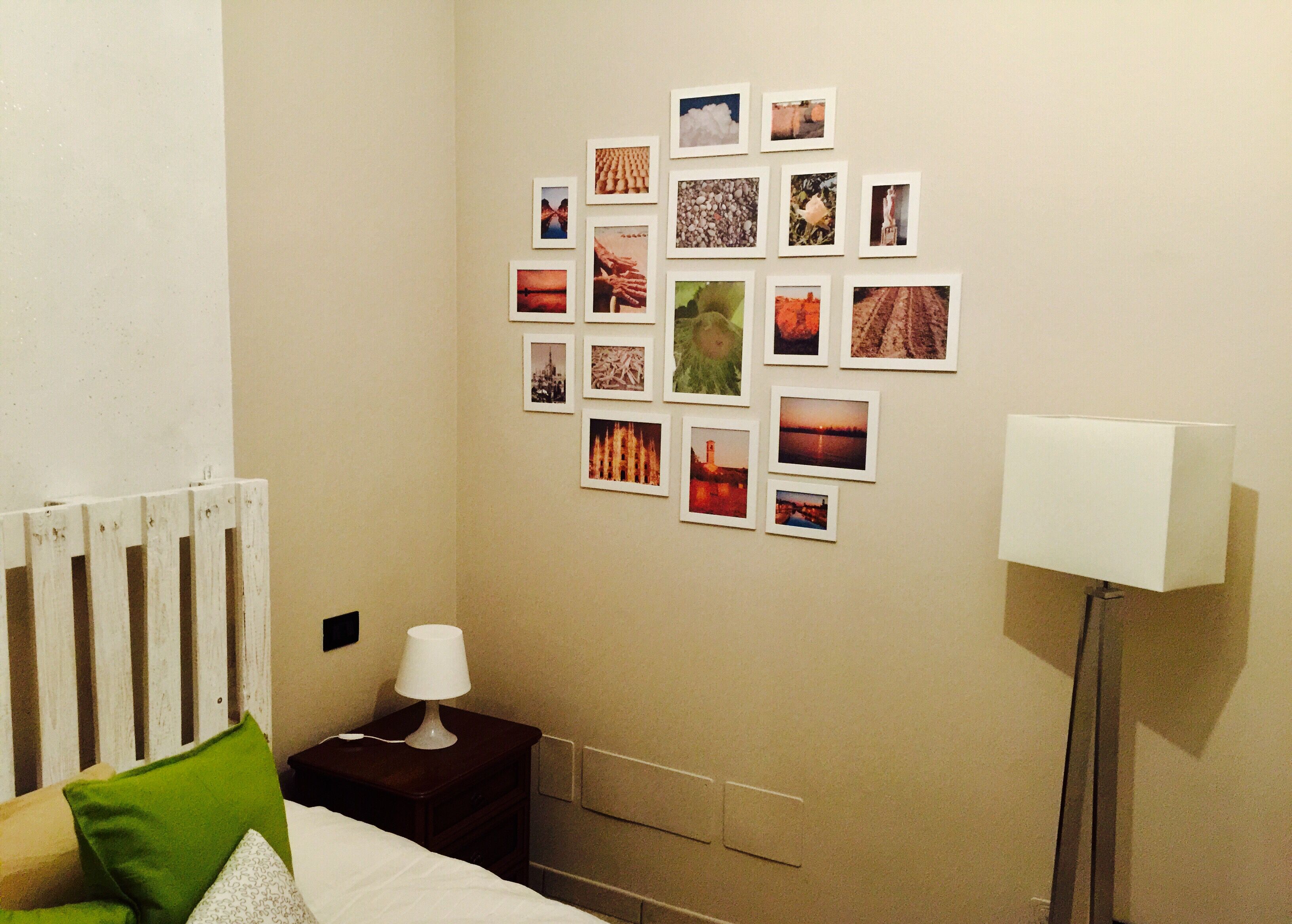 A hotel room with a bed, a nightstand with a lamp, a wall decorated with photos, and a floor lamp.