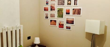 A hotel room with a bed, a nightstand with a lamp, a wall decorated with photos, and a floor lamp.