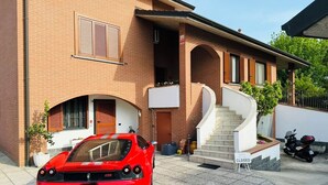 Un coche deportivo rojo estacionado frente a una casa de ladrillo con una escalera que lleva a la entrada.