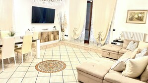 Una sala de estar con sofá, televisión, lámpara de araña y alfombra estampada.
