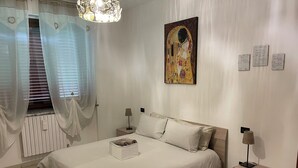 Un dormitorio con cama, mesitas de noche, cortinas en una ventana, un cuadro colgado en la pared y un radiador.