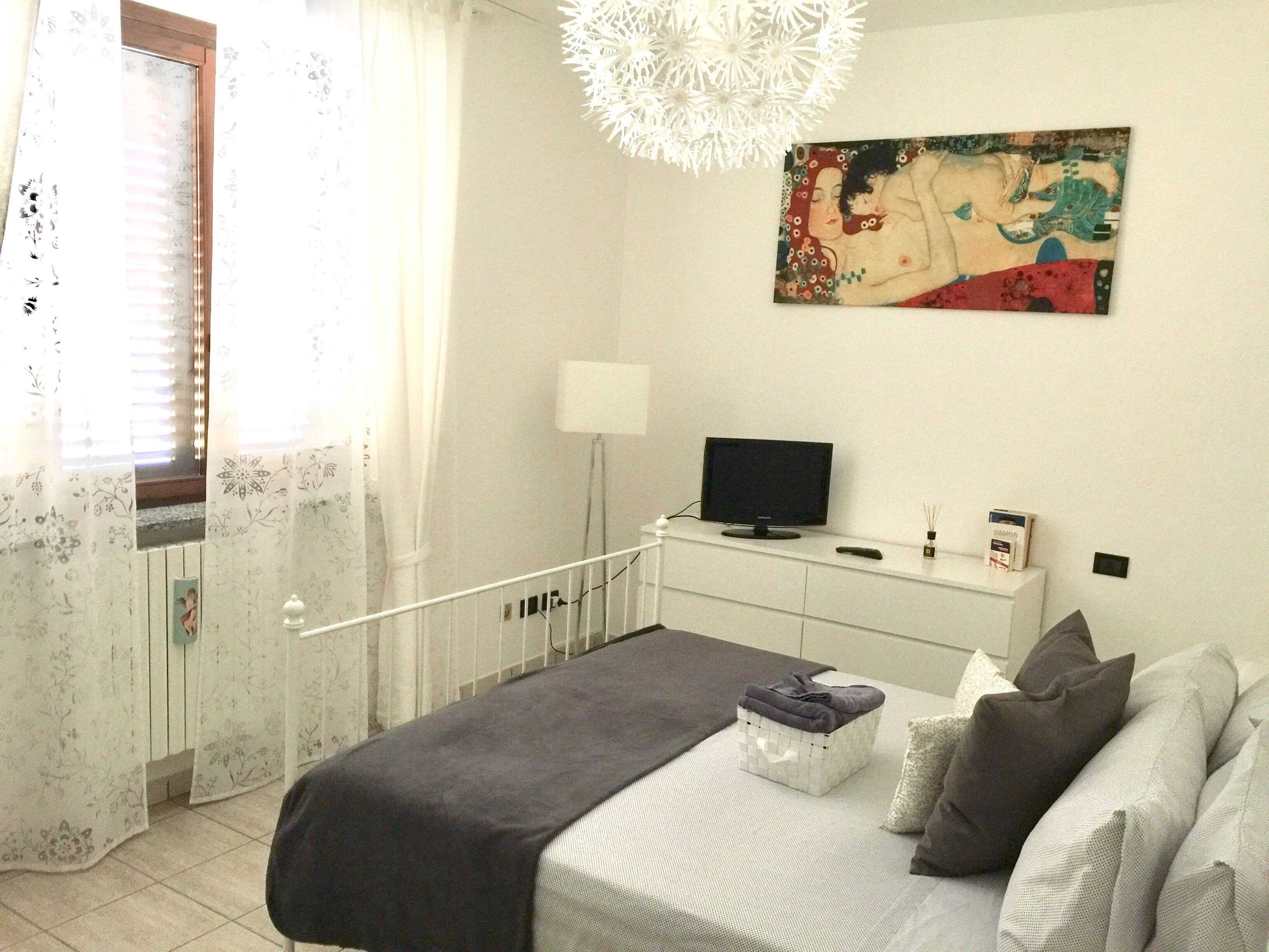 Un dormitorio con cama, televisor, mesita de noche, lámpara y un cuadro en la pared.