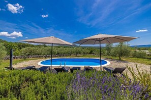 Une piscine entourée de verdure et de collines, avec des chaises longues et des parasols.
