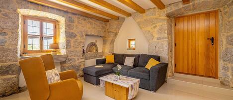 A cozy living room with a stone wall, wooden beams, a sofa, a chair, and a fireplace.