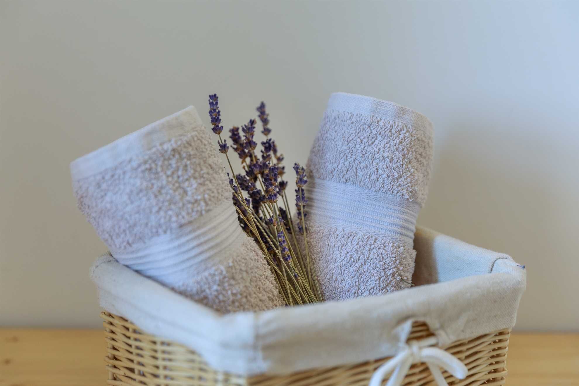 A wicker basket containing folded towels and a sprig of lavender.