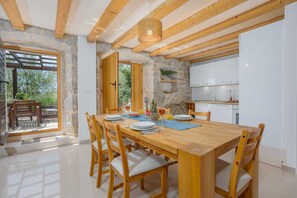Een eetgedeelte met een houten tafel en stoelen, een keuken met witte kasten, en een stenen muur.