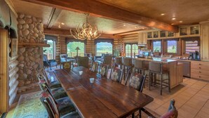 A spacious log cabin with a large dining area, kitchen, and a stone fireplace. - Luxurious Hillside Lodge on a Working Wyoming Ranch (Little Jackson Hole)