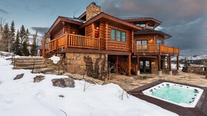 A log cabin with a stone foundation, wooden balconies, and a hot tub in the snow. - Luxurious Hillside Lodge on a Working Wyoming Ranch (Little Jackson Hole)