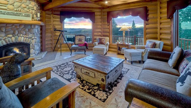 A log cabin interior with a stone fireplace, a wooden coffee table, and a sofa set. - Luxurious Hillside Lodge on a Working Wyoming Ranch (Little Jackson Hole)