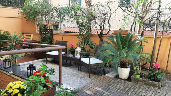 Eine Terrassenfläche mit Gartenmöbeln, Blumentöpfen und einem Tisch mit einer Laterne.