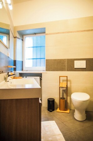 Ein Badezimmer mit Waschbecken, Spiegel, Fenster, Toilette und Mülleimer.