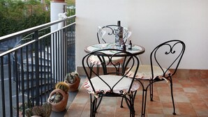 Un balcón con una mesa redonda, dos sillas, una botella de vino y tres cactus en macetas.